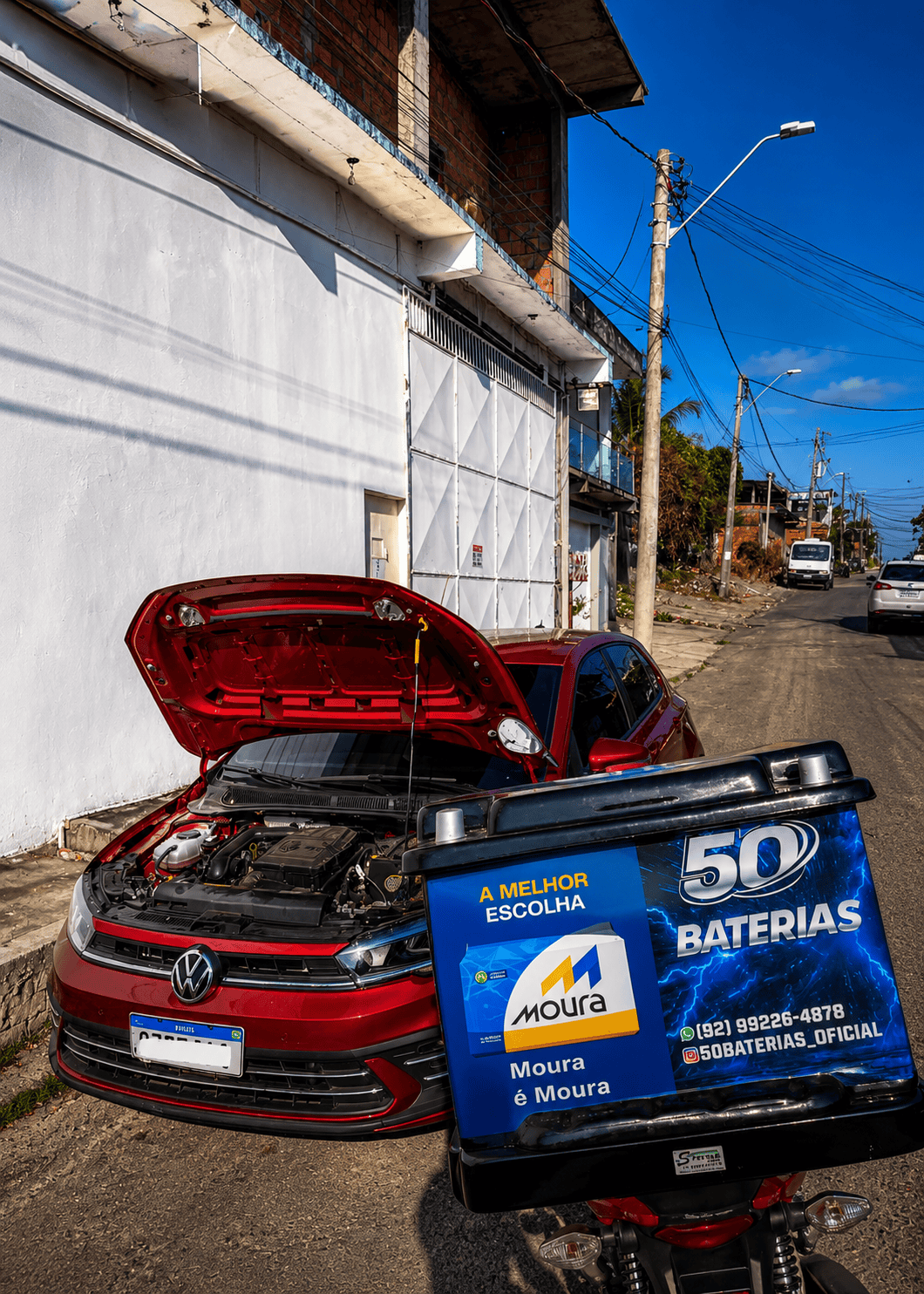 Entregador da 50 Baterias atendendo um veículo na rua, com bateria e caixa de transporte da marca